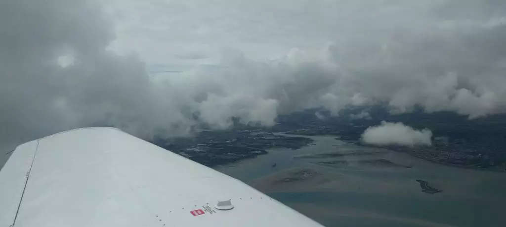 Clouds surrounding our PA-28 over a natural harbour and land.